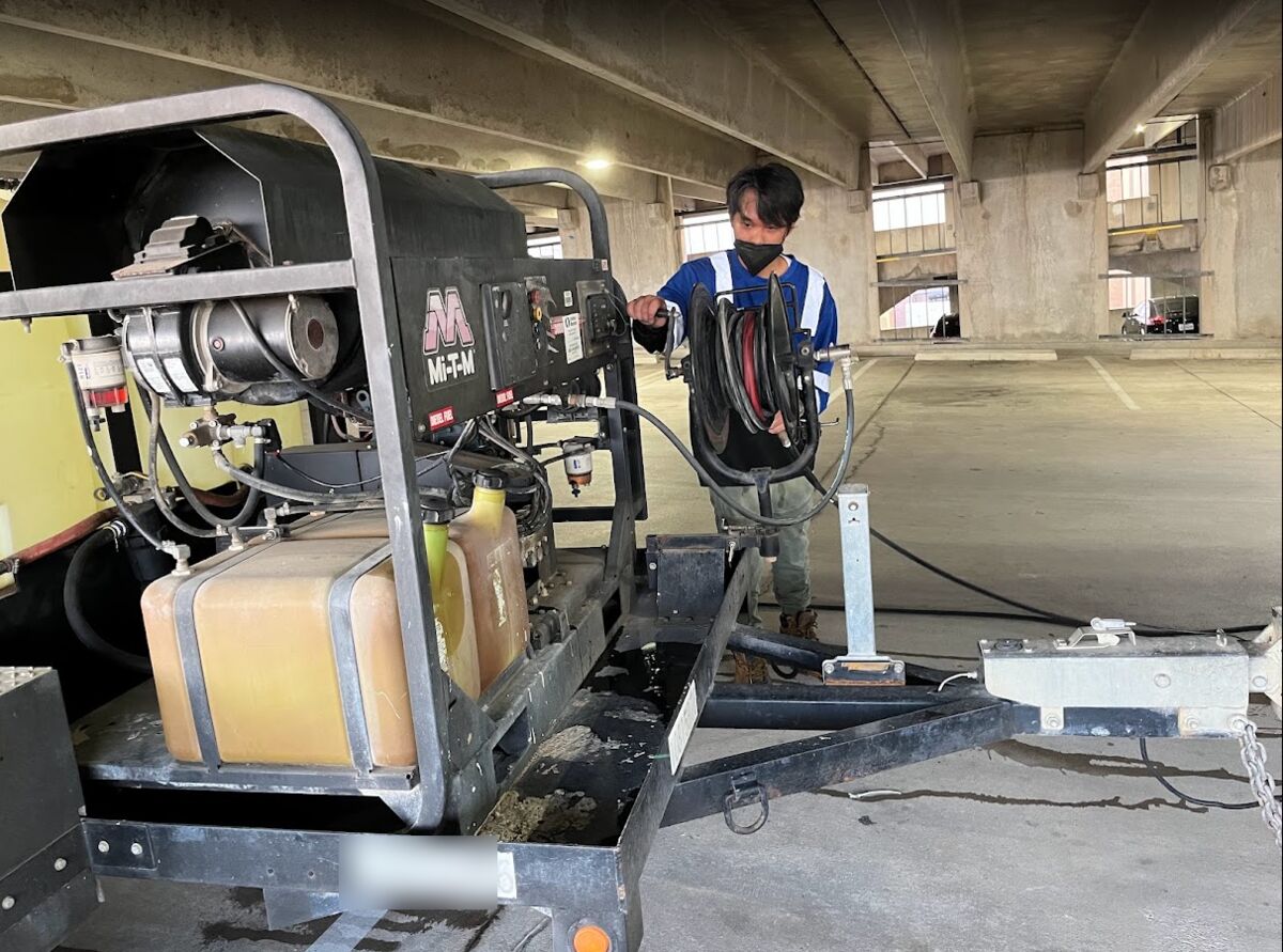 Crew member setting up the hose reel on a trailer-mounted hot-water pressure washer inside a parking garage