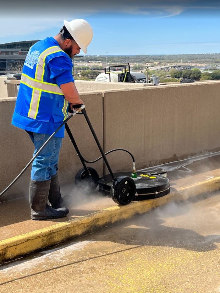 Crew member running a surface cleaner along a curb, steam rising