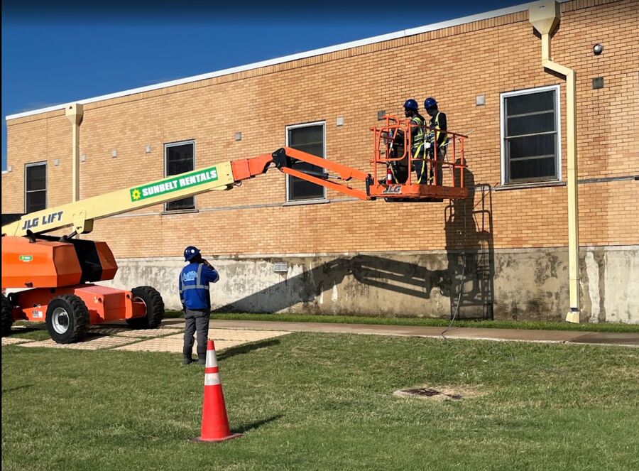 Crew in a boom lift washing the upper brick wall of a building while a spotter works the ground