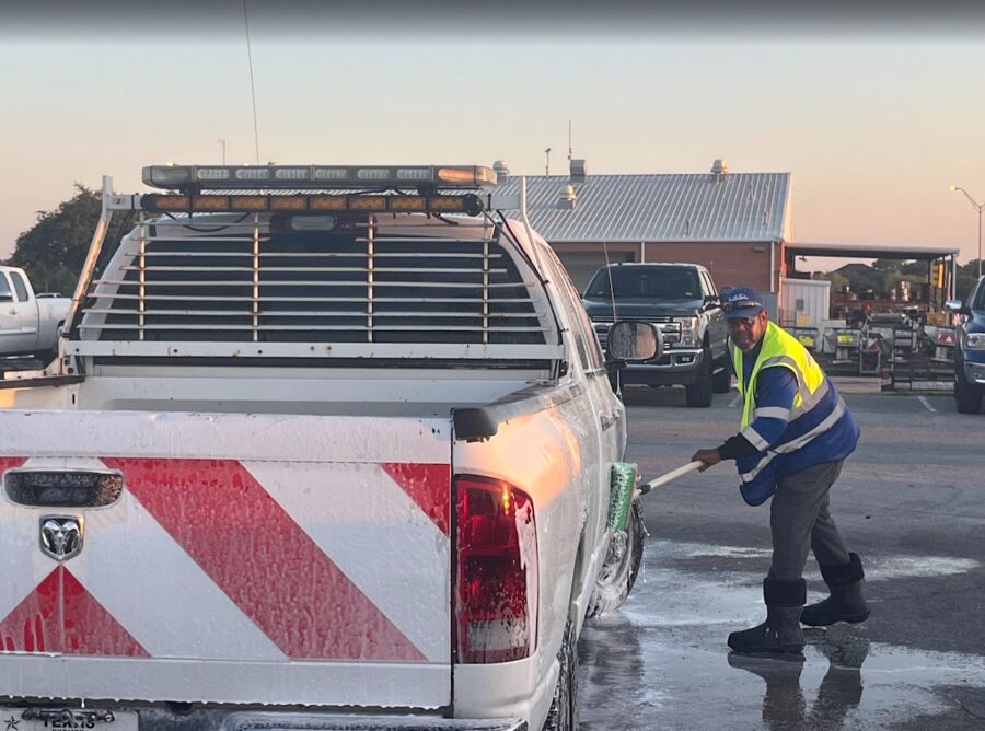 Crew member foam-washing a Texas Department of Transportation pickup at sunrise